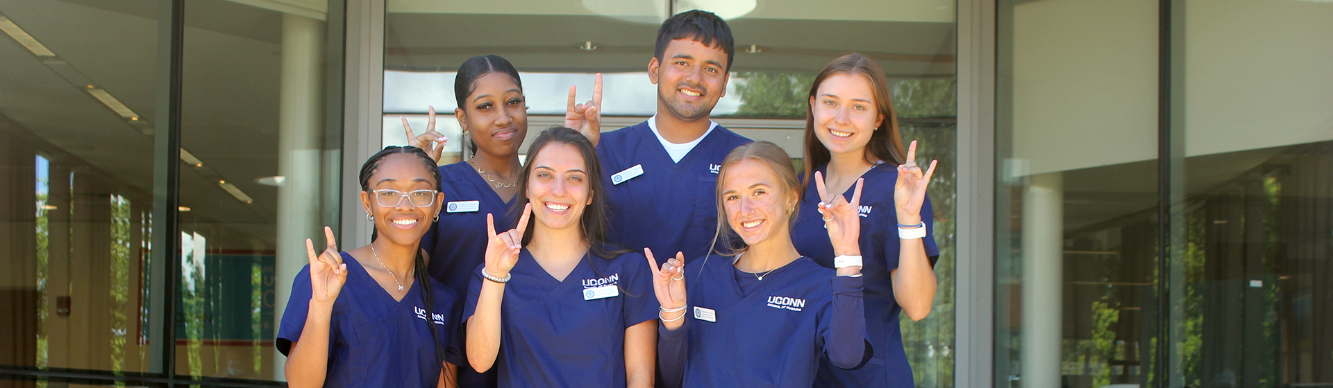 A group of six students wearing blue scrubs making Husky sign