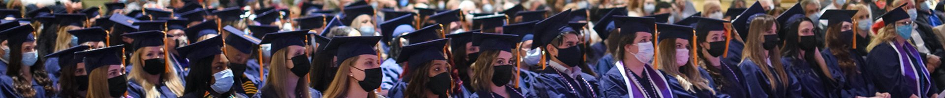 Graduates sit in an auditorium in caps and gowns