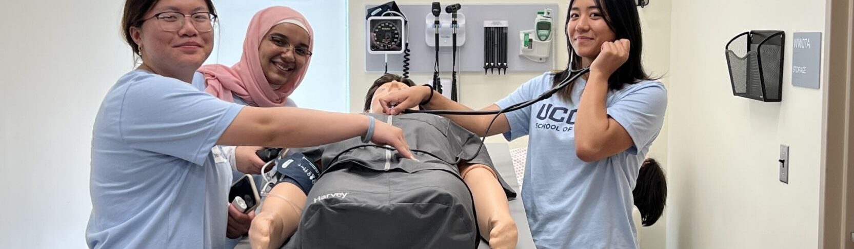 EINP Summer 2023 in the Sim Lab - three female students taking pulse of manikin with stethoscope